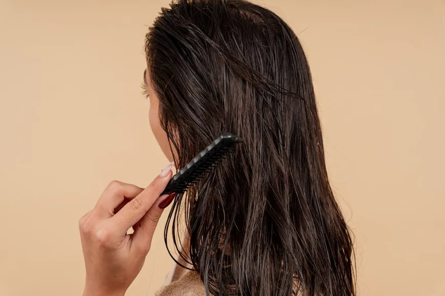 Woman brushing long hair while managing hereditary hair loss and thinning hair.