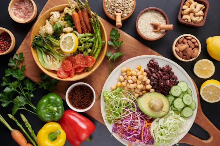 Healthy vegetarian meal bowls with fresh vegetables, avocado, beans, chickpeas, sprouts, and colorful salad ingredients arranged on a dark table with nuts, seeds, and lemons