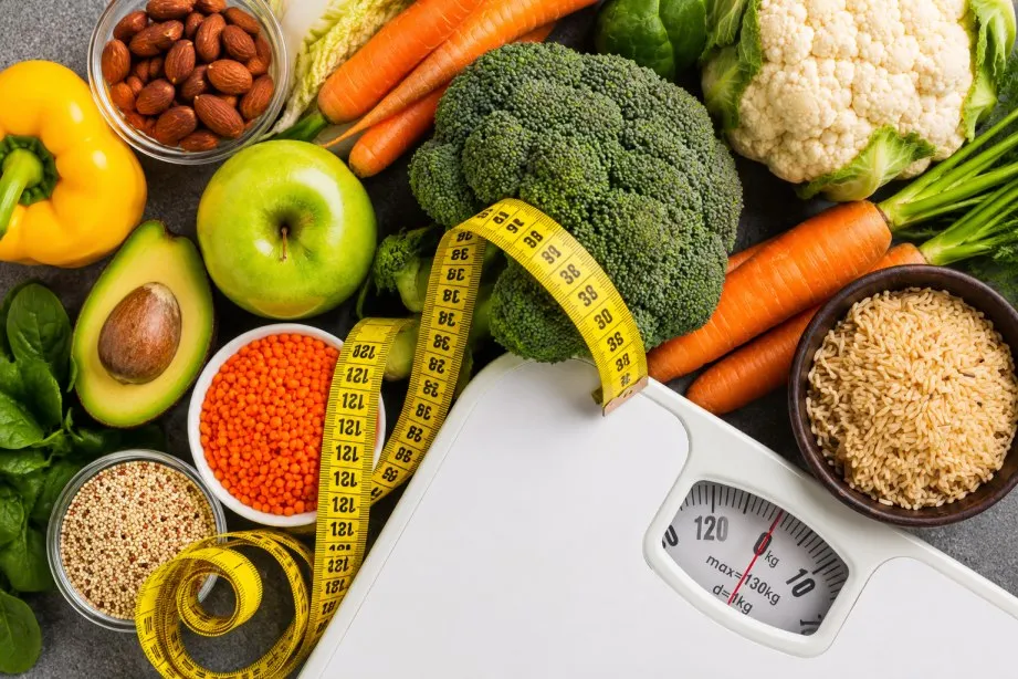 “Flat lay of healthy foods, vegetables, grains, and a weighing scale with measuring tape representing balanced nutrition, weight management, and healthy lifestyle choices