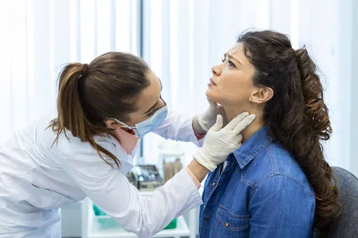 Female doctor examining a young woman’s neck and thyroid area during a medical consultation in a clinic